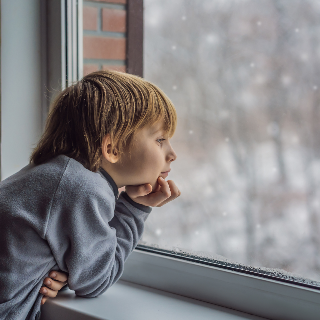 child looks out of window on snow scene 